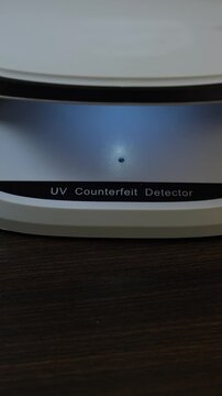 Examination of Uzbekistan Sum (UZS) cash money with UV counterfeit detector. Concept of authenticity check, fight against counterfeiting of banknotes, anti fraud measures in Uzbekistan. Close up view.