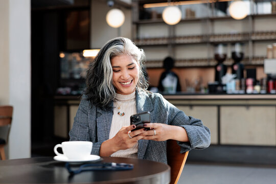 Woman smiles at mobile phone in cafe with coffee.