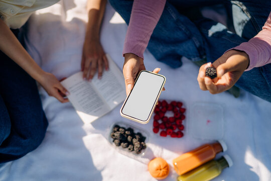A woman's hand with a white-screen mobile phone during a picnic