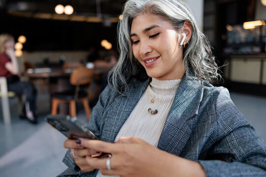 Smiling woman with gray hair using mobile phone at cafe