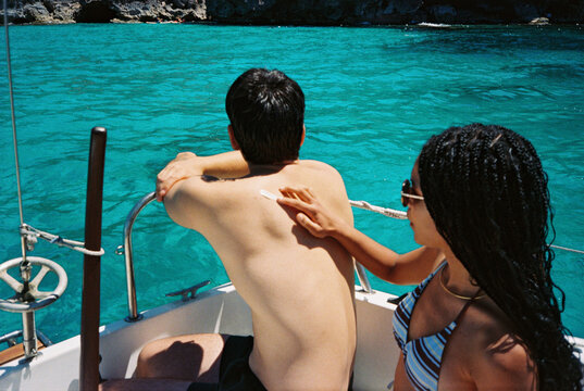 Candid summer portrait of couple applying sunscreen at sea