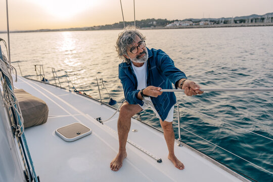 Mature man pulling rope on sailboat at sunset