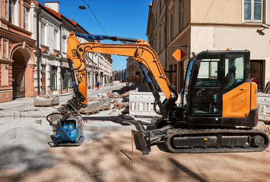 Mini excavator with hydraulic plate compactor working on road construction in an old European town street
