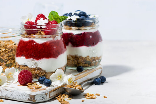 sweet desserts with granola, berry and fruit puree in jars on white wooden board