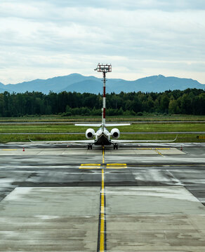 Rear view of a private aircraft aligned on a rain soaked airport apron with dramatic mountain backdrop and expansive cloudy sky creating balanced aviation composition with copy space