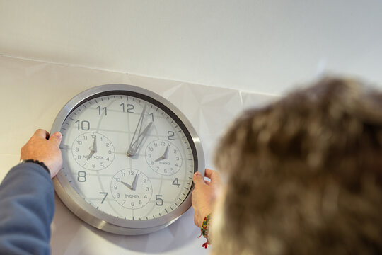 Close view of a person adjusting a wall clock for the seasonal daylight saving time change in spring or autumn to make better use of daylight.