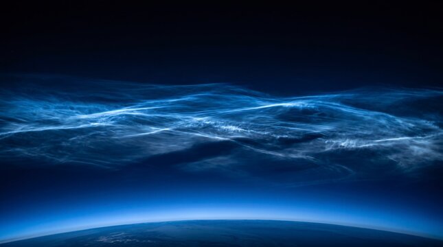 Stunning view of noctilucent clouds glowing brightly above the curved horizon of earth in the deep blue mesosphere during the twilight hours of a quiet night in outer space
