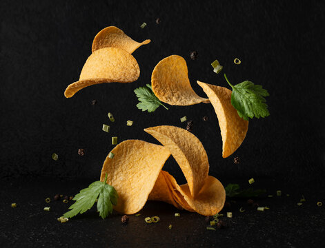 Flying potato chips with herbs and allspice on black background