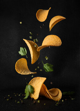 Flying potato chips with herbs and allspice in the air on black background
