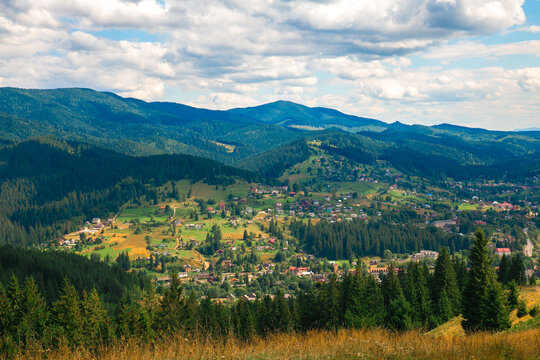 Picturesque mountain landscape. Ukrainian Carpathians. A cozy village lies in the valley below, surrounded by rolling green hills and misty mountain peaks. Bright traditional houses and untouched