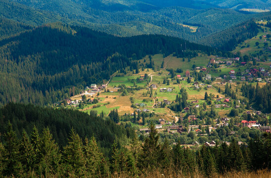 Picturesque mountain landscape. Ukrainian Carpathians. A cozy village lies in the valley below, surrounded by rolling green hills and misty mountain peaks. Bright traditional houses and untouched