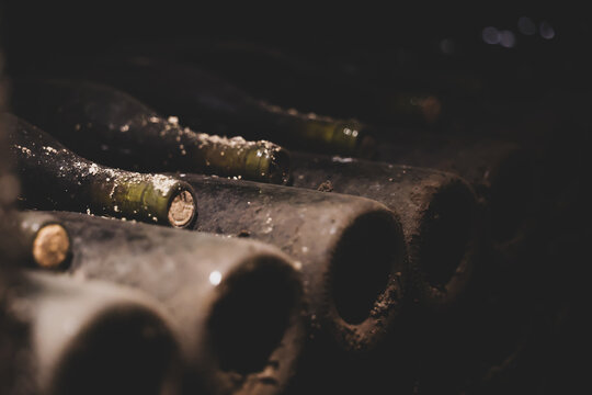 A close-up of dusty wine bottles stored horizontally in a dark cellar, evoking age, tradition, and the passage of time.