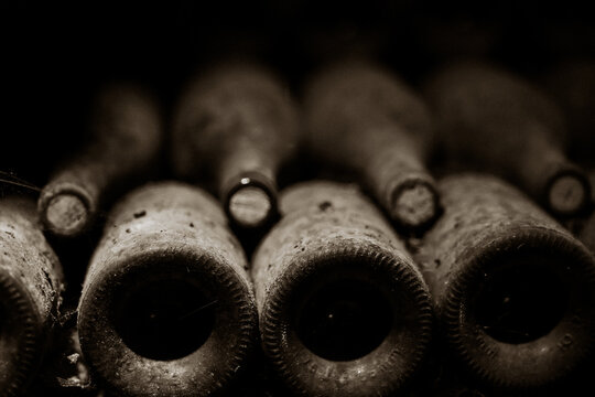 A close-up of aged wine bottles in low light, their dusty surfaces and muted tones emphasizing timeless craftsmanship.
