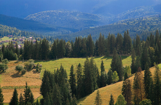 Picturesque mountain landscape. Ukrainian Carpathians. A cozy village lies in the valley below, surrounded by rolling green hills and misty mountain peaks. Bright traditional houses and untouched