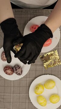 Woman's hands decorating easter eggs with gold leaf
