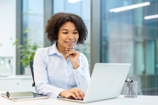 Smiling young African American businesswoman sitting in the office and working on a laptop