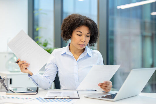 Concentrated young African American woman sitting at a desk in the office and working with documents