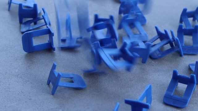 Blue plastic clamps for tile leveling system, close-up. Professional consumables for laying ceramic and porcelain tiles. A large number of blue plastic clamps fall on a gray surface. Repair