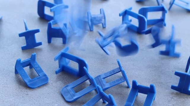 Blue plastic clamps for tile leveling system, close-up. Professional consumables for laying ceramic and porcelain tiles. A large number of blue plastic clamps fall on a gray surface. Repair