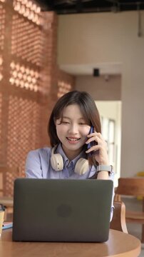Young Asian Businesswoman Working Remotely with Laptop and Smartphone in Traditional Wooden Cafe, Digital Nomad Lifestyle