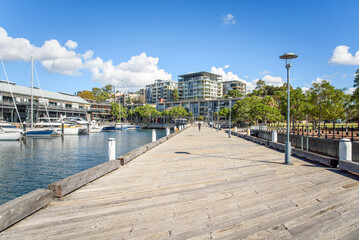 Fototapeta premium Modern apartment buildings in a waterfront development on a sunny autumn day. A wooden pier and moored boats are in foreground. 