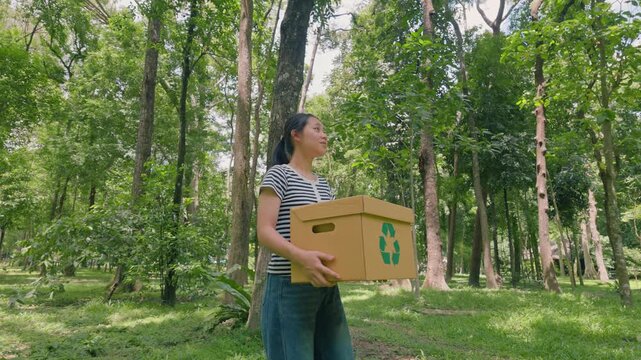 Asian woman holding recycling box on green nature forest background. Sustainable environment concept. Recycle plastic free of zero waste, from waste to environment. 