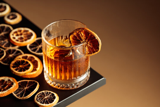 Old-fashioned cocktail with ice and a dried orange slice.