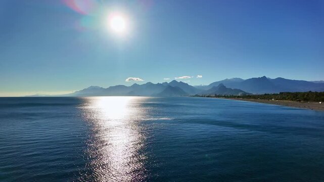 Bright sun glare reflecting on calm mediterranean sea with taurus mountains and coastline in antalya.