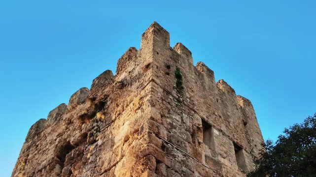 Weathered ancient stone fortress wall with battlements rising against clear blue sky in antalya.