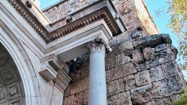 Detailed view of ancient corinthian marble column beside weathered stone wall at hadrian's gate antalya.