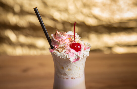Creamy pink milkshake topped with whipped cream and a red cherry, served with a black straw. Sweet cold dessert drink with a rich creamy texture.