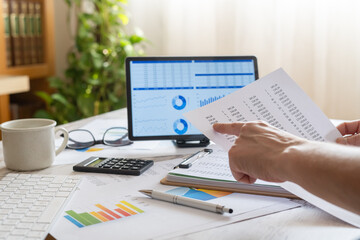 Fototapeta premium Business person comparing data on a printed financial report with digital charts and spreadsheets on a computer screen, managing workflow and reviewing accounting tasks