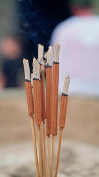 Burned incense sticks in upright bundle with curling blue smoke rising gently through soft diffused light and dark charred tips, creating calm spiritual mood with subtle texture and vertical