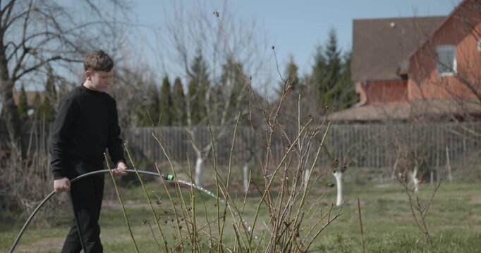 Kid Waters Plants in Garden Near House. Caucasian Boy Help Working Around Backyard. 4K 10-bit