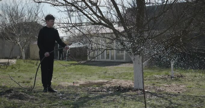 Kid Waters Plants in Garden Near House. Caucasian Boy Help Working Around Backyard. 4K 10-bit