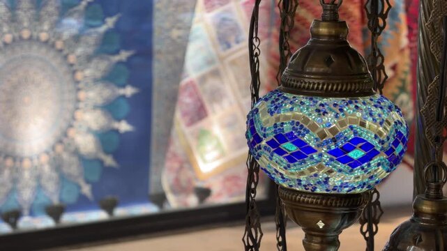 Close-up shot of an ornate Turkish mosaic lamp casting a glowing light in a traditional bazaar with colorful patterned tapestries in the background in Istanbul, Turkey.
