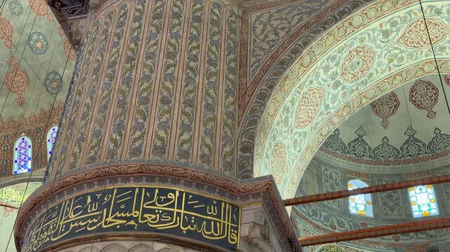 Slow tilt up shot revealing the ornate calligraphy, intricate floral tile work, and monumental architectural columns inside the Blue Mosque in Istanbul, Turkey.