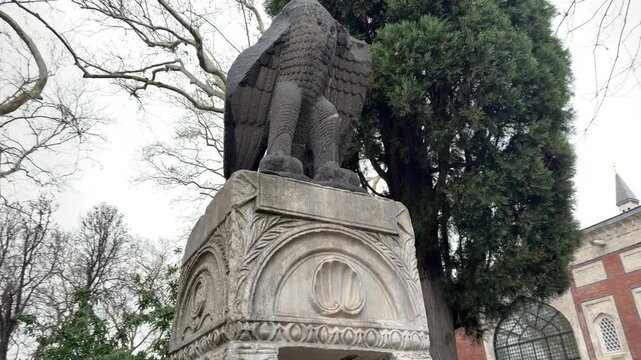 Low angle shot of a weathered stone eagle statue perched on an ornate base at the historic park grounds surrounding the Topkapi Palace in Istanbul, Turkey.