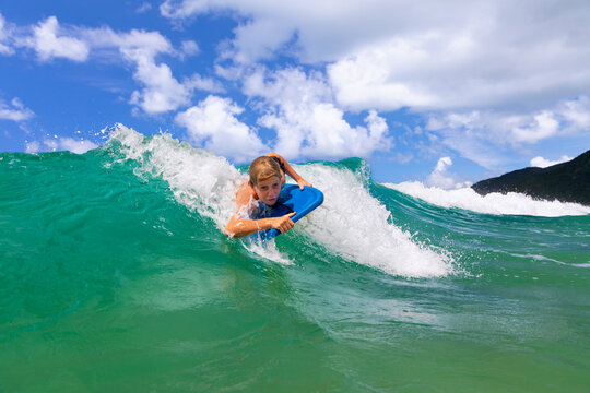 Happy young surfer boy with bodyboard have fun on beach, riding on small ocean waves. Summer adventures, active families, parents and kids lifestyle, sports activities on school holiday with kids