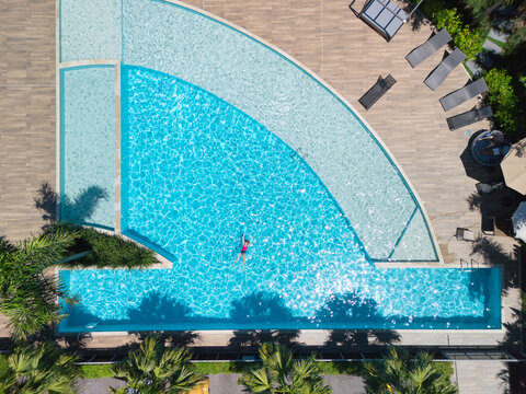 Young girl swimming in clear blue pool during sunny summer vacation. This aerial view captures family,  friends, fun, and recreation at resort, relaxation and joyful outdoor moments.