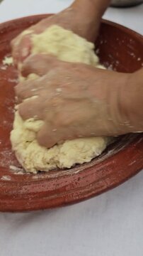 Close-up video of hands mixing and kneading dough ingredients in a traditional Moroccan clay bowl (Gsaa) to make dough for Rfissa.
