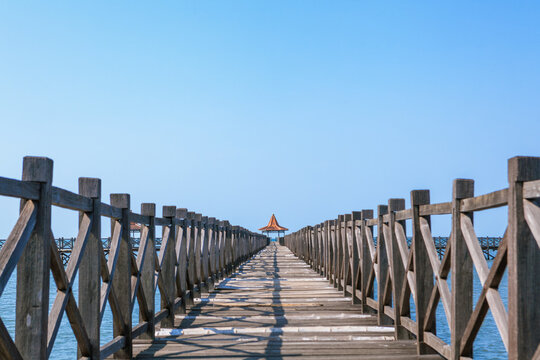 Long wooden pier with traditional gazebos - bale stretches over calm turquoise sea under clear blue sky. Perfect place for viewing amazing landscape.  Scenery for travel, resort, summer vacation