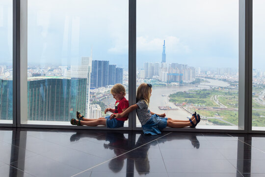 Funny kids look at panoramic view of Ho Chi Minh City from modern skyscraper&rsquo;s observation deck. Urban lifestyle, travel with kids, and high-rise cityscape concept with Southeast Asian charm.