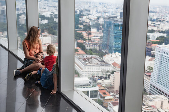 Woman, two children look at panoramic view of Ho Chi Minh City from modern skyscraper&rsquo;s observation deck. Urban lifestyle, travel with kids, and high-rise cityscape concept with Southeast Asian charm.