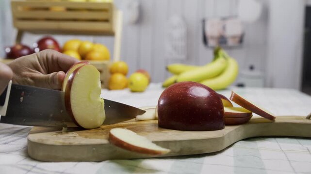 Cook using sharp knife to cut apple into smaller slices on cutting board in kitchen, closeup