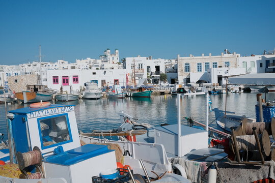 Panoramic harbor view of Naousa, Paros, Greece, with traditional fishing boats, calm blue waters, and whitewashed Cycladic buildings on a sunny summer day.