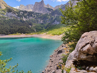 A large boulder and rocky shore frame a vibrant turquoise alpine lake with dramatic rocky mountains rising in the background. © stanhert
