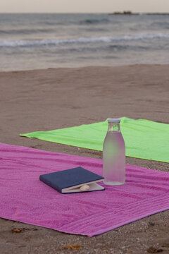 Vertical beach towels with book and glass water bottle by sea