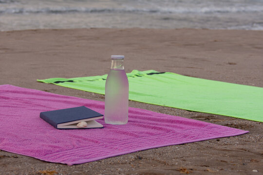 Beach towels with book seashell and glass water bottle by the sea