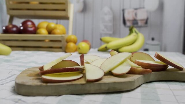 Tracking shot near red apple slices on wooden cutting board in kitchen - closeup